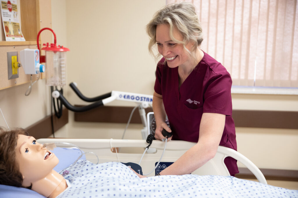 A smiling nursing student works on a practice dummy in the nursing lab