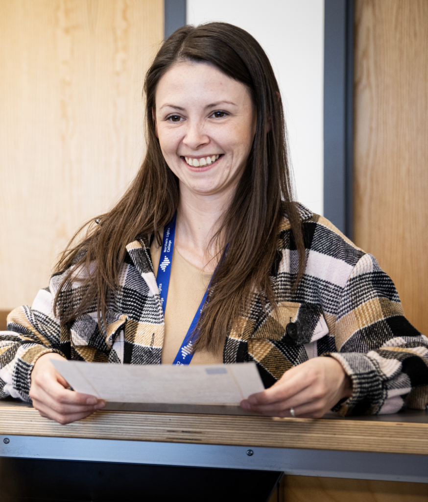 Student standing at counter with paper in hand and smiling