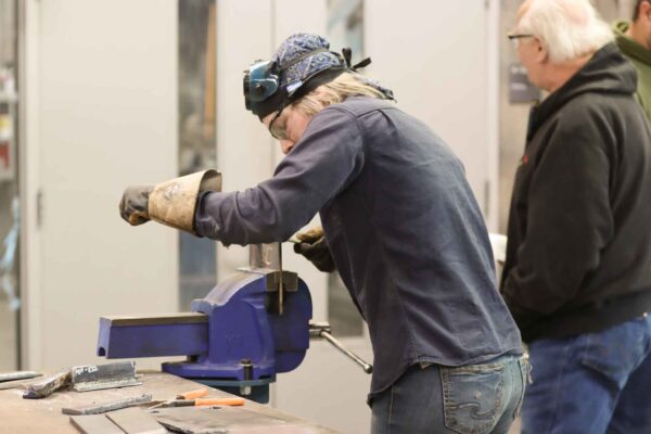 a female student grinds a welding plate that is held in a table clamp