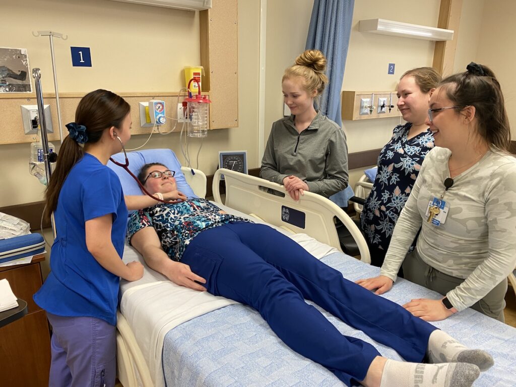 Healthcare students gathered around one student using a stethoscope on another