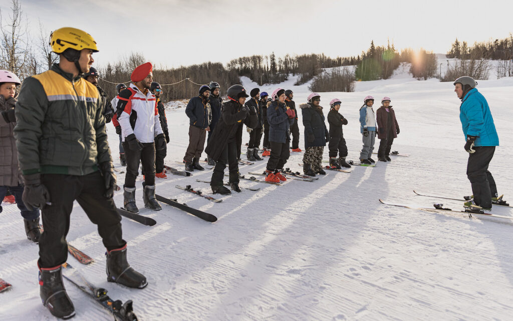 Lineup of students on skis at the skihill listening to instructor