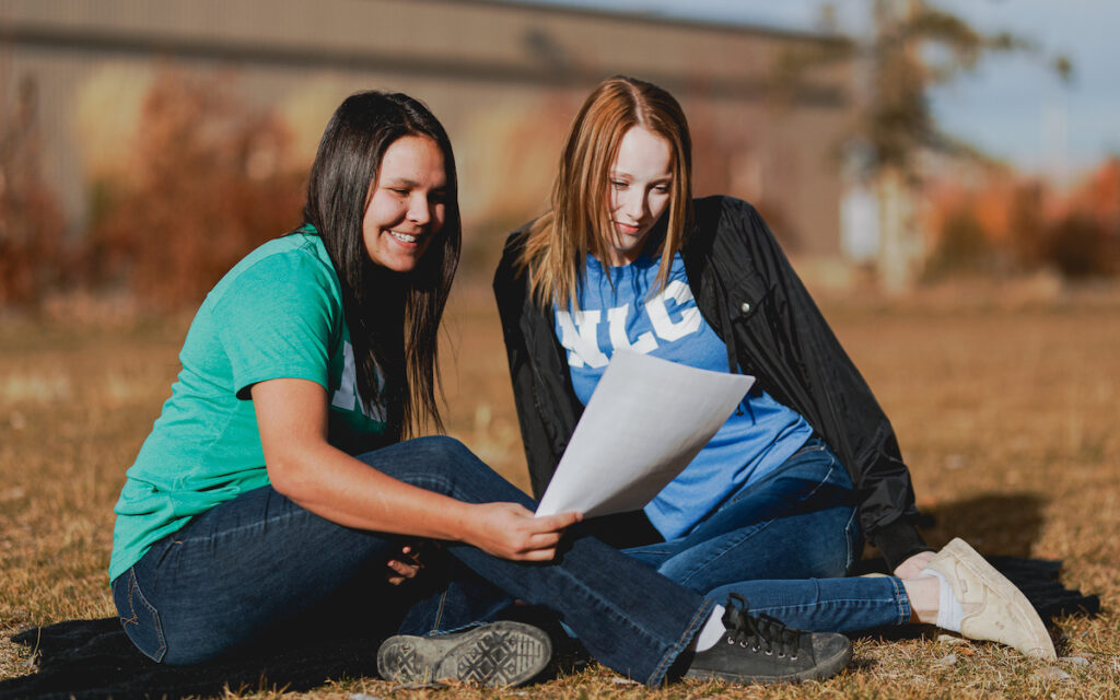 Two NLC students sitting on grass and looking at piece of paper together