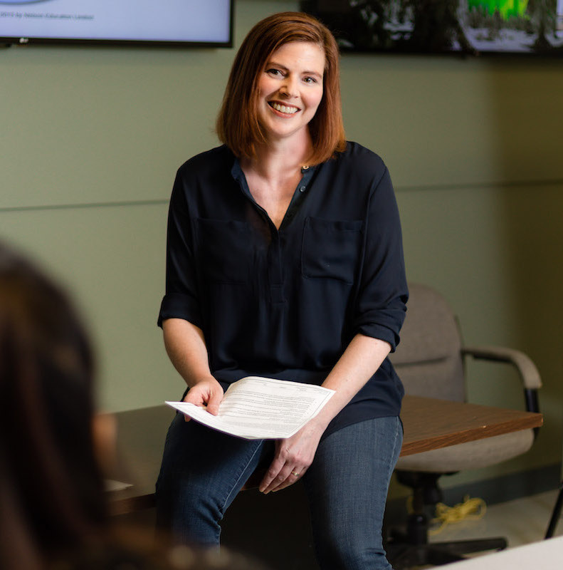 Professor sitting on table with papers in hand and smiling