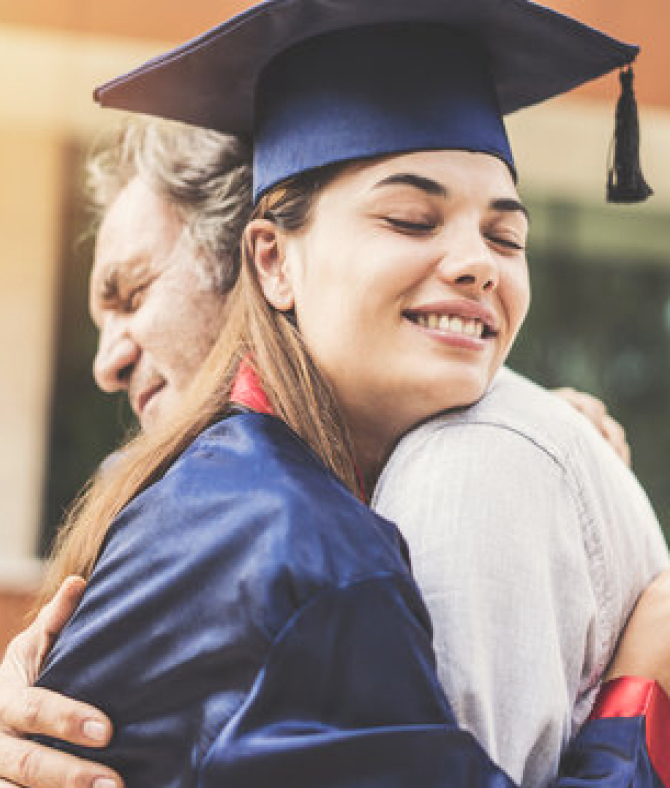 Young woman in graduation gown hugging her father at NLC graduation