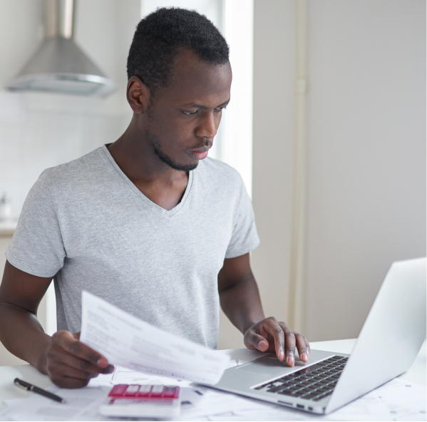 Student looking at laptop with paper and calculator in hand